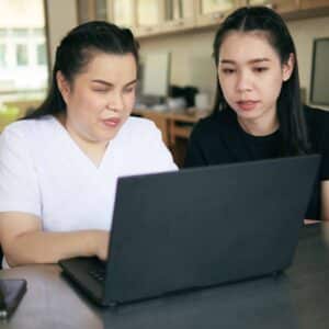 Asian women co-workers in workplace including person with blindness disability using laptop computer with screen reader program for visual impairment people. Disability inclusion at work concepts