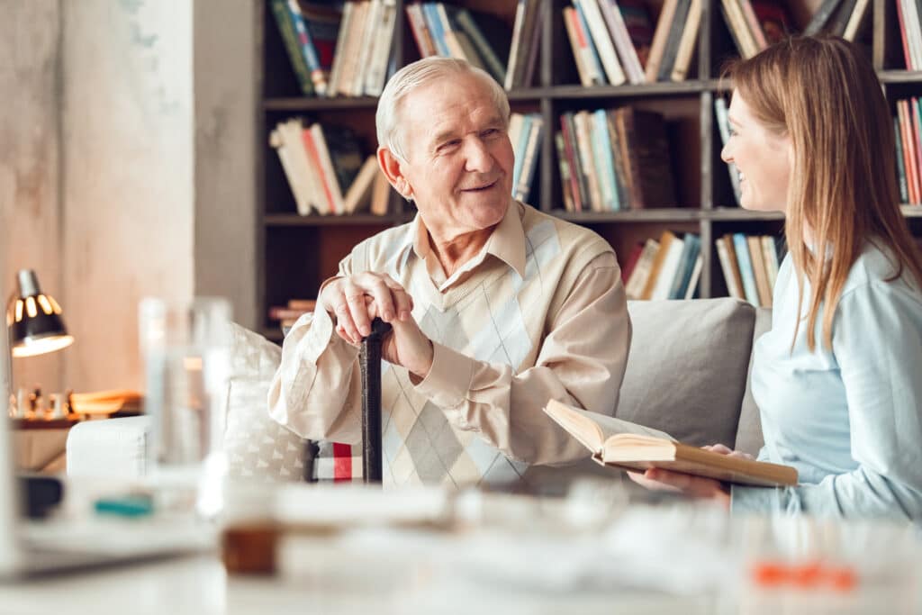 Father and daughter at home library sitting man looking at woman holding book laughing man with cane talking with friend